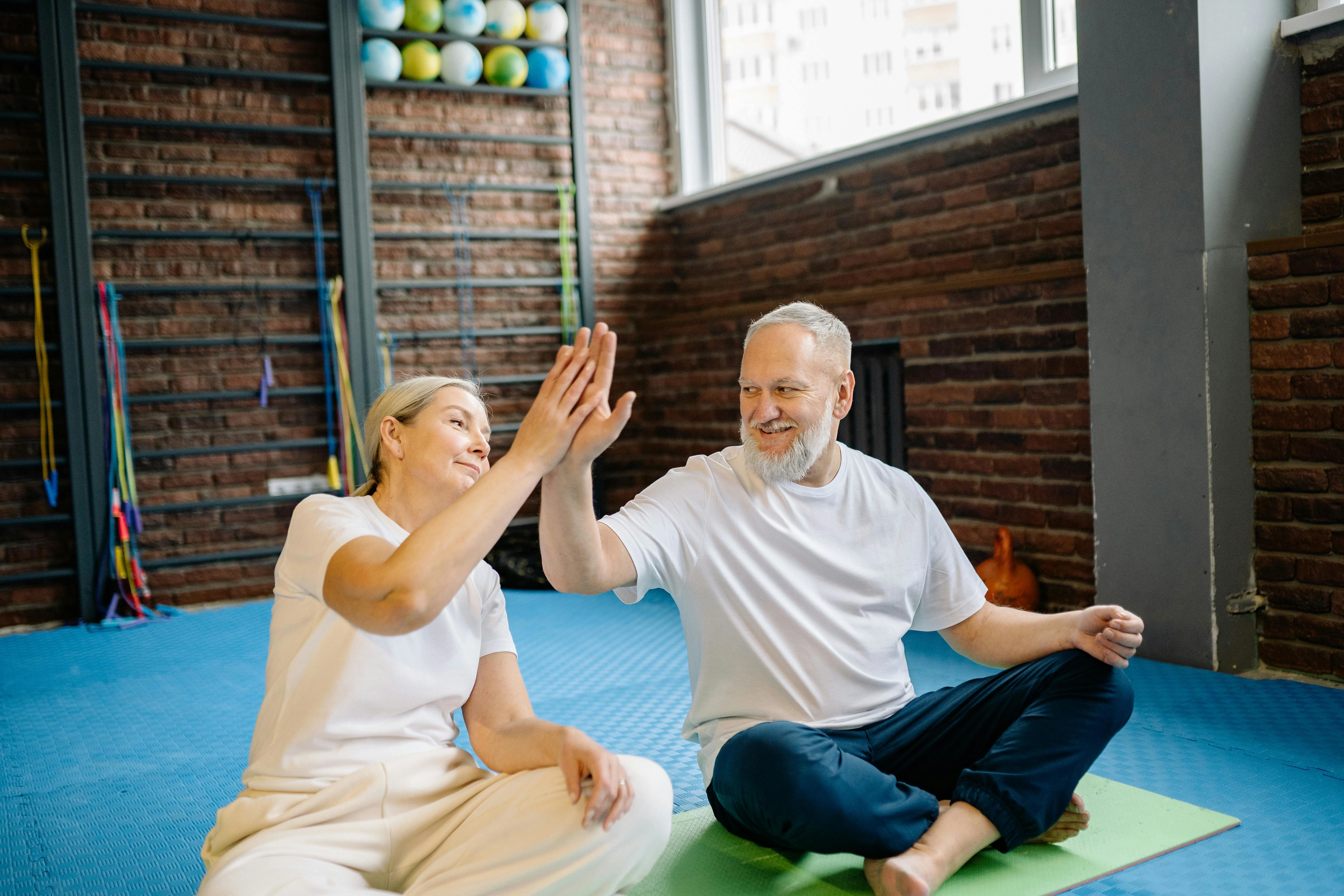 Twee mensen, patiënten van Foot Care Center by Spronken Orthopedie, geven elkaar high five in gymzaal